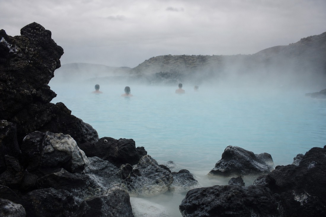 Milky turquoise water and drifting steam at the Blue Lagoon with bathers in the distance among dark lava rocks