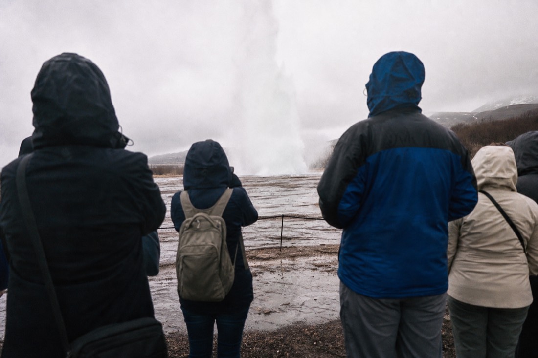 Travelers waiting around the Strokkur geyser vent at Geysir as steam rises before an eruption