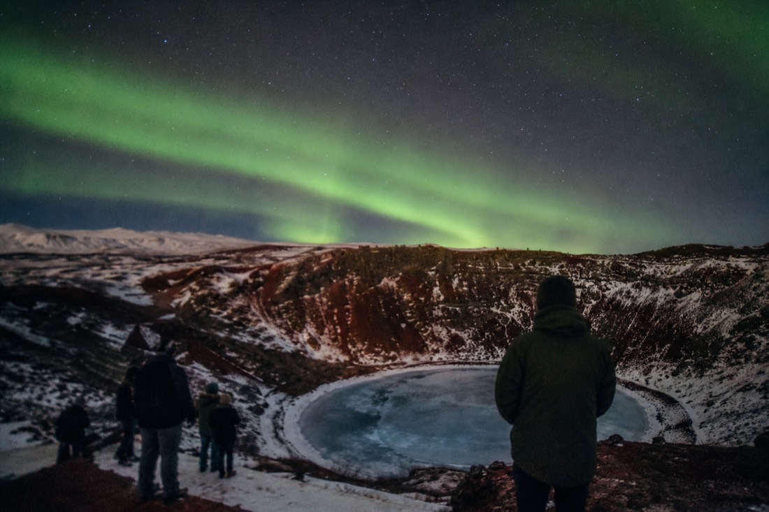 Green aurora arcing over the snowy rim of Kerið crater on a clear winter night