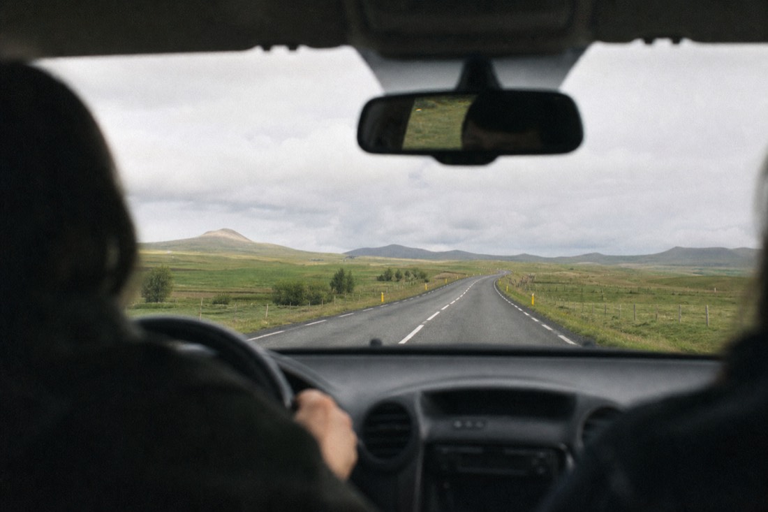 Rental car on the empty paved loop road through green farmland near Laugarvatn under soft cloud