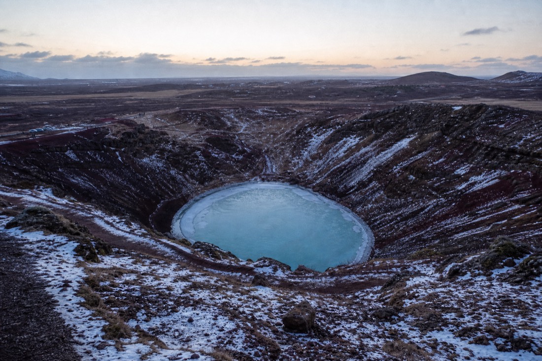 Red volcanic slopes and frozen turquoise lake inside Kerið crater at winter dusk