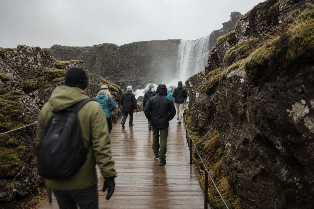 Boardwalk leading toward Öxarárfoss waterfall between mossy lava walls on an overcast day