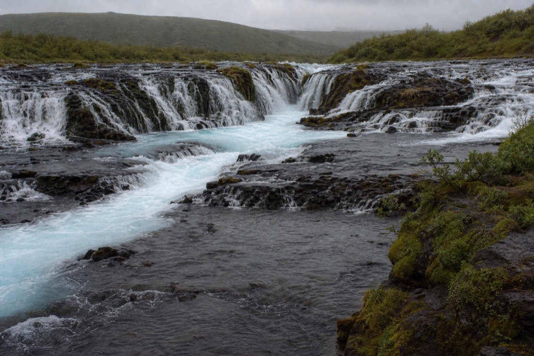 The bright blue cascades of Brúarfoss waterfall running over shallow rock ledges