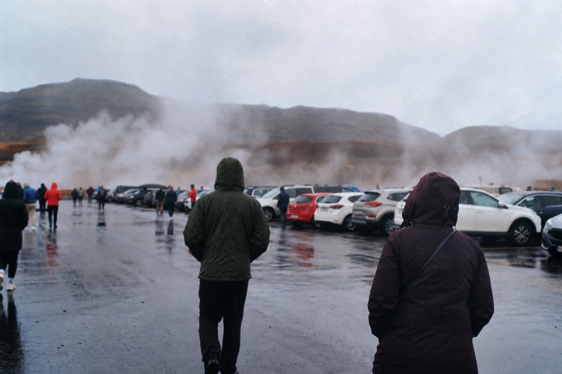 Steam from the Geysir geothermal field drifting over parked cars in the roadside car park