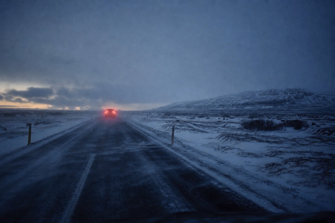 Snow blowing across Route 36 near Þingvellir at winter dusk with tail lights ahead