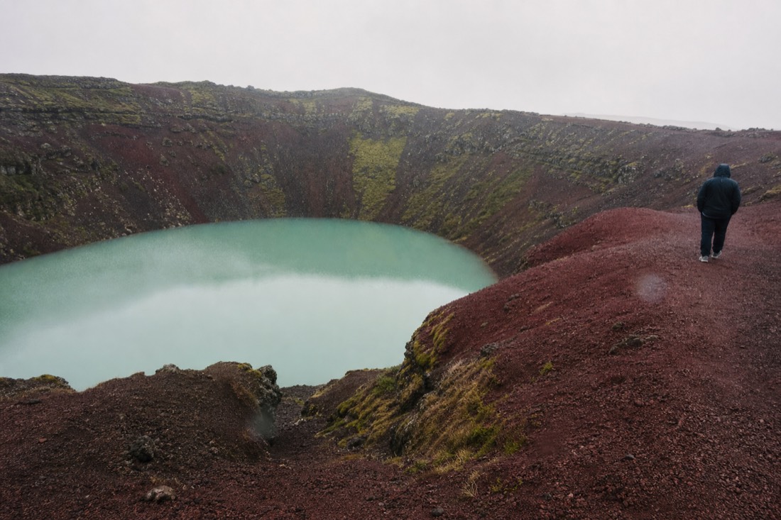 Red volcanic rim of Kerið crater circling its green lake in drizzle