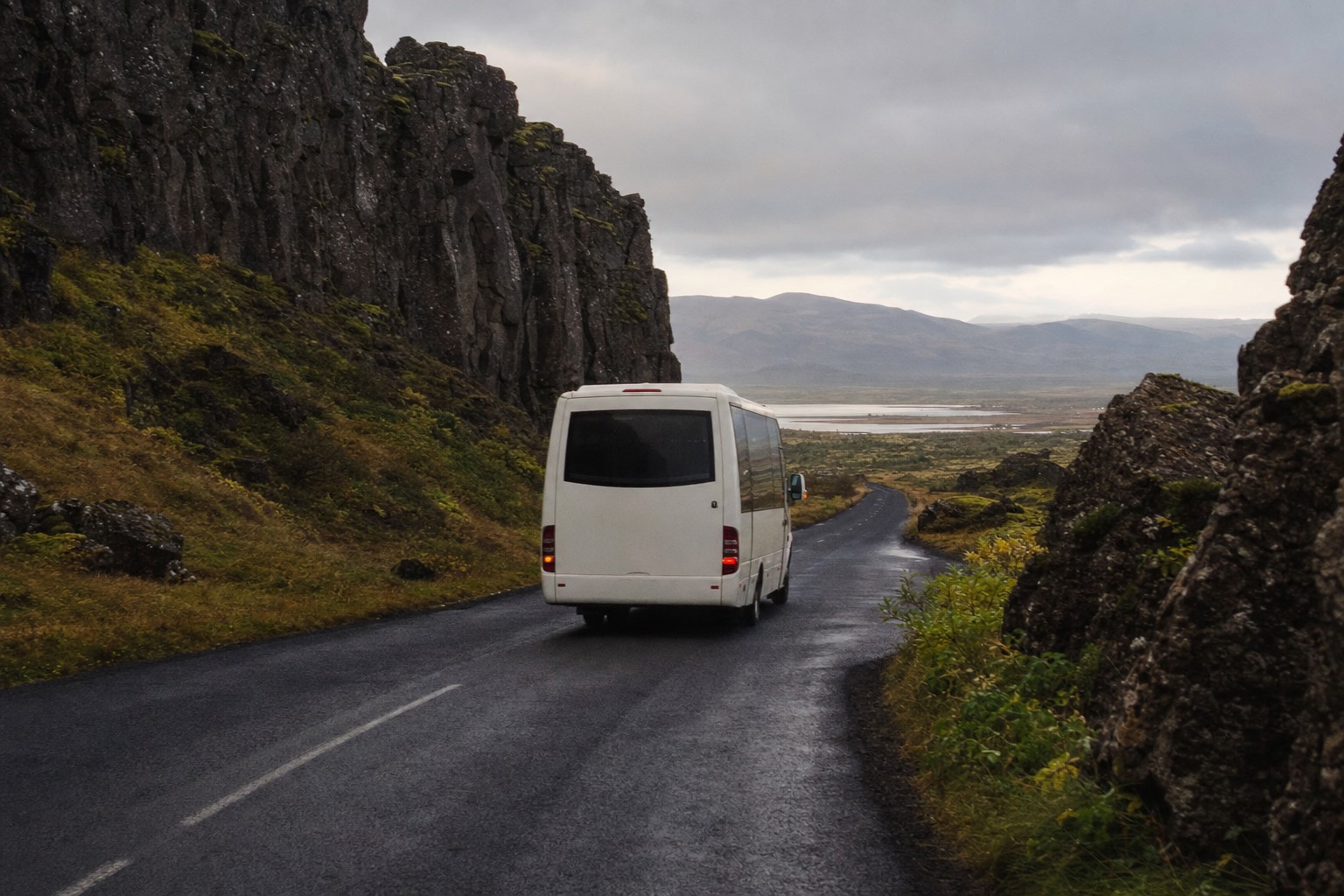 Unbranded white tour minibus on the empty road through the Þingvellir rift valley in low morning light