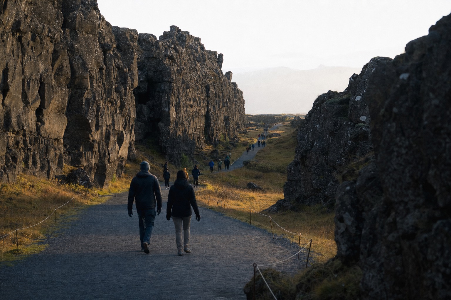Gravel path running through the Almannagjá gorge at Þingvellir with dark basalt walls rising on both sides under low morning light