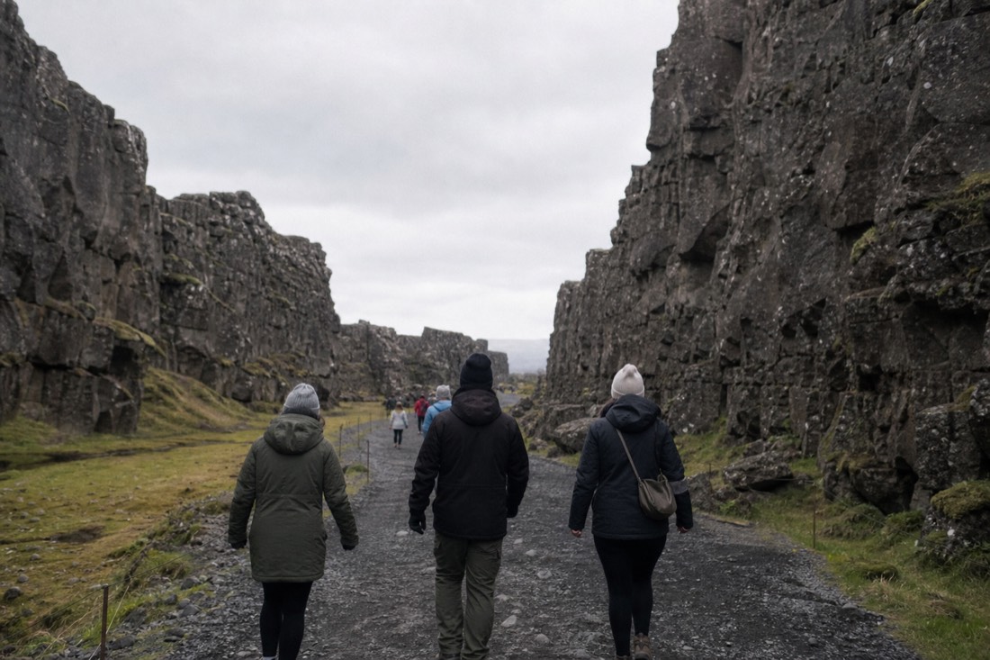 Visitors walking the wide gravel path along the floor of Almannagjá gorge at Þingvellir, seen from behind