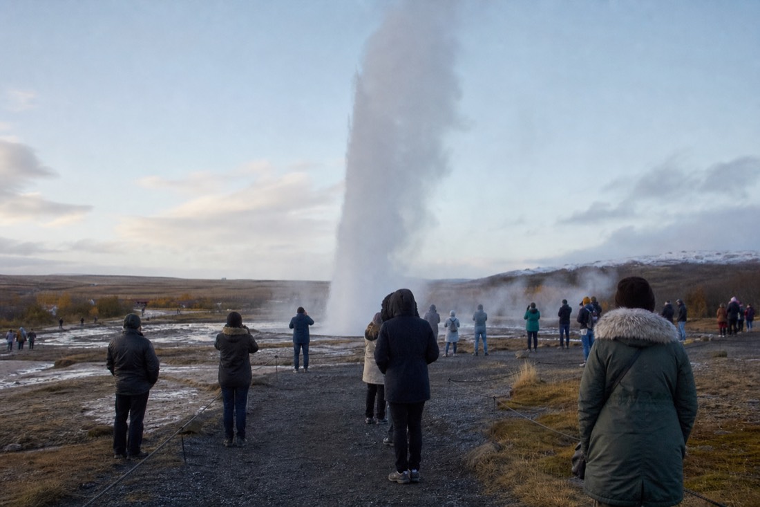 Steam column from Strokkur geyser rising over a thin morning crowd at Geysir